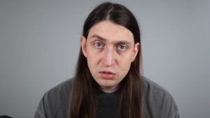 Imagem de um homem em fundo cinza, com expressão preocupada e olhar direto para a câmera, transmitindo tensão e possível desconforto emocional associado à fobia social.