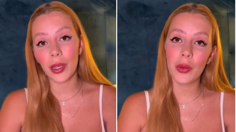 Malévola Alves em close, olhando para a câmera, com maquiagem suave e batom rosado, usando top branco de alça fina e colar delicado, em fundo escuro.
