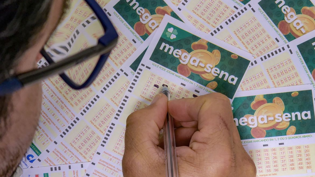 Jogo de loteria com bilhetes do tipo “mega-sena” e mão segurando uma marcação, com cartões preenchidos e números impressos.