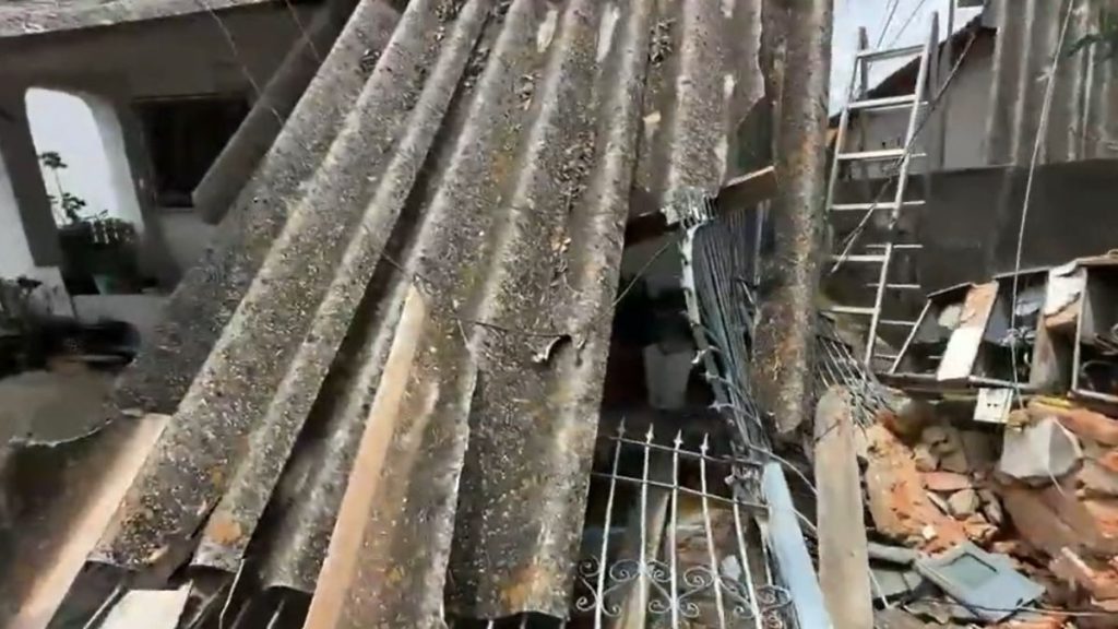 Telhado de fibrocimento destruído e escombros na entrada de uma residência após acidente com contêiner em Americana.