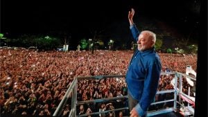 Lula acena para multidão durante evento político noturno com milhares de apoiadores.