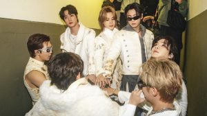 Foto do BTS com integrantes em roupas brancas, em um ambiente interno, posando juntos e encarando a câmera, em clima de bastidores