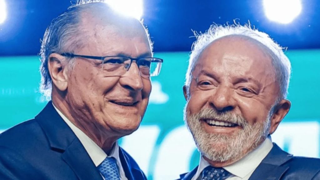 Luiz Inácio Lula da Silva e Geraldo Alckmin aparecem sorrindo juntos, usando ternos e gravatas azuis durante evento político.