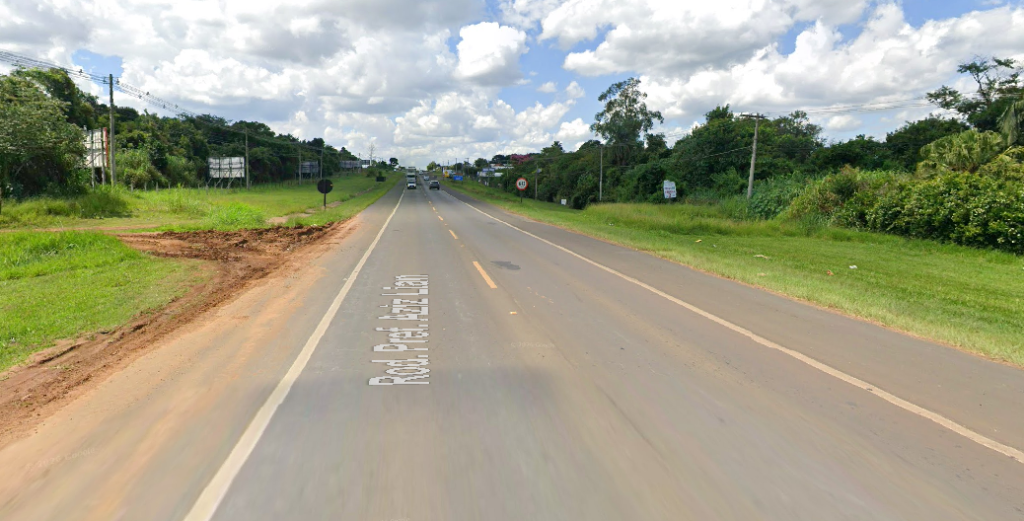 Rodovia SP-107 em Holambra, com pista asfaltada, faixas ao centro, vegetação nas laterais e céu parcialmente nublado ao fundo.