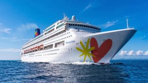 Navio de cruzeiro branco com bandeira colorida “Bem-vista” e grande coração ao lado, navegando no mar azul sob céu claro.