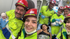 Equipe de paramédicos usando capacetes vermelhos e macacões amarelos em ambiente hospitalar, com pessoas sorridentes e uma paciente sendo atendida com materiais de primeiros socorros.