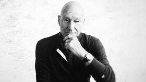 Ator Patrick Stewart posa para retrato em preto e branco, com a mão apoiada no queixo.