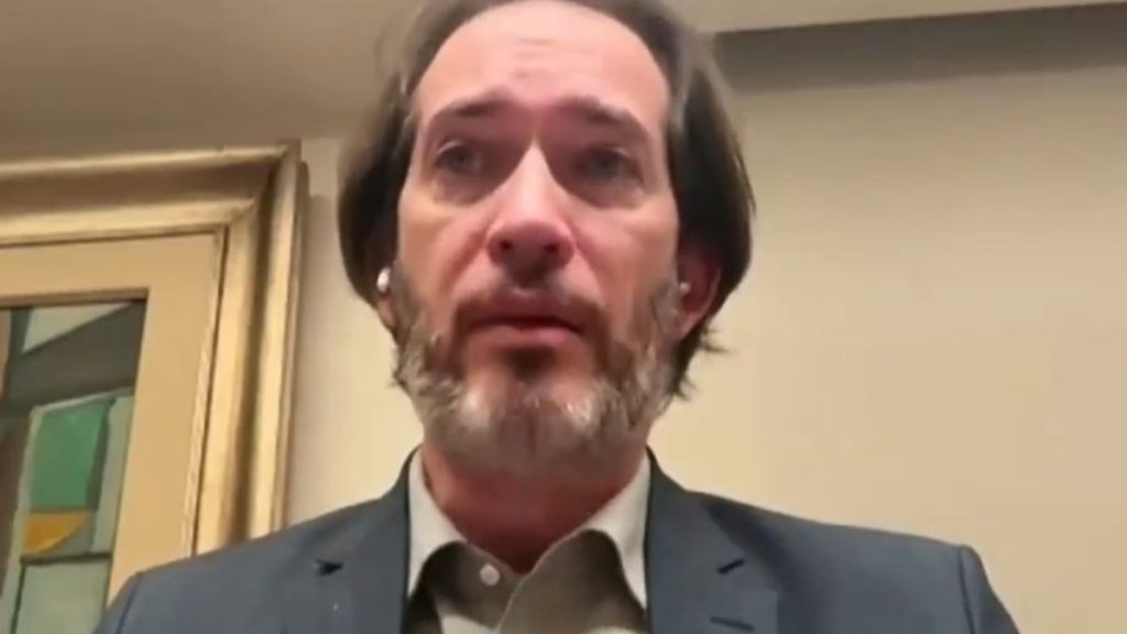 Plano aproximado do advogado criminalista Pierpaolo Bottini a falar numa videoconferência, usando fato escuro, camisa clara e fones de ouvidos brancos.