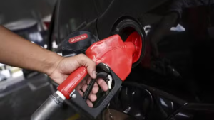 Abastecimento em posto de gasolina: mão inserindo a bomba vermelha na entrada do tanque do carro, com registro de “GASOLINA” visível.