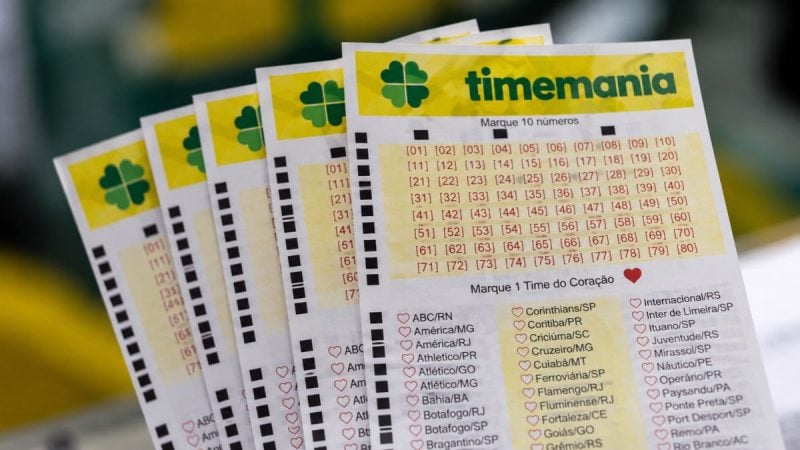 Timemania: cartões de bilhetes com a marca Timemania e tabela de números para marcação, com listas de times e corações no papel.